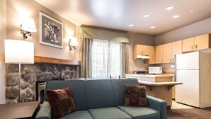 A modern living room with a sofa, a dining table, and a kitchen area with wooden cabinets and appliances. - Quality Inn & Suites Bainbridge Island (Bainbridge Island)