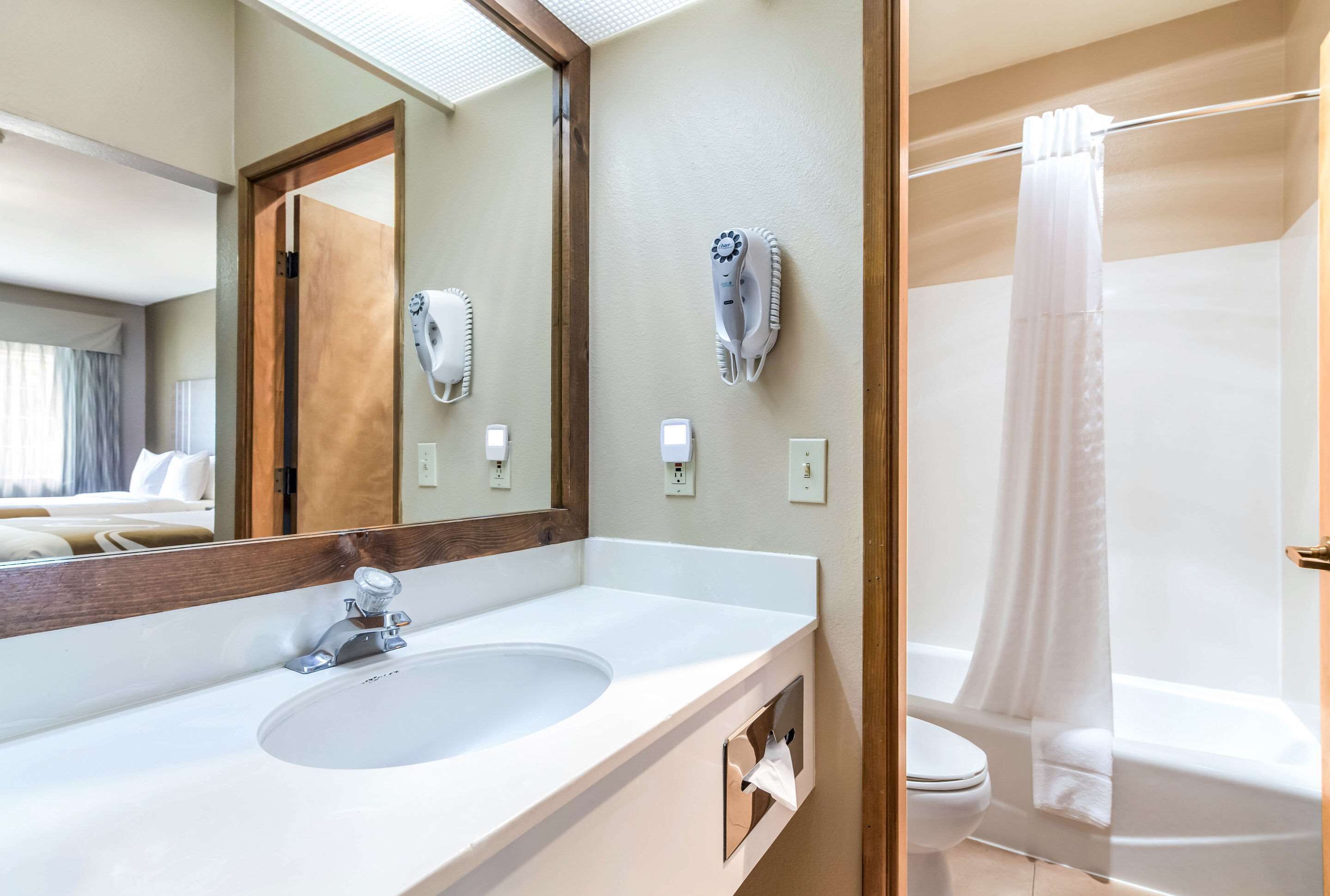 A modern bathroom with a large mirror, a sink, a hairdryer, and a shower curtain.