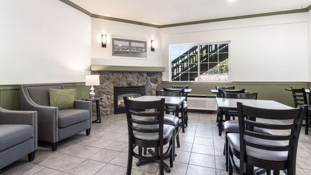 A dining area with a stone fireplace, multiple tables and chairs, and a view of a building through a large window. - Quality Inn & Suites Bainbridge Island (Bainbridge Island)
