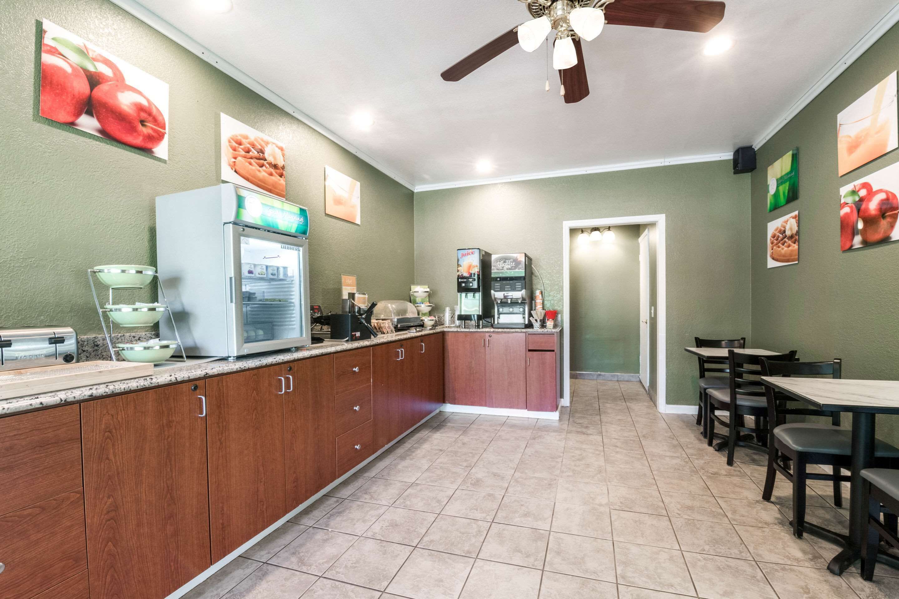 A kitchen with wooden cabinets, a refrigerator, a coffee machine, and a microwave. There are also several framed pictures on the walls.