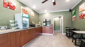 A kitchen with wooden cabinets, a refrigerator, a coffee machine, and a microwave. There are also several framed pictures on the walls.