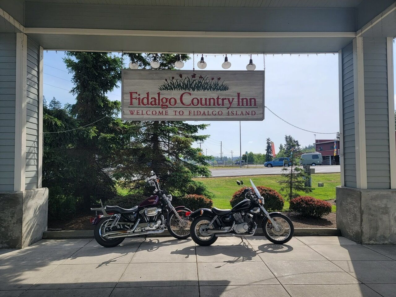 A sign for Fidalgo Country Inn welcoming to Fidalgo Island with two motorcycles parked outside.