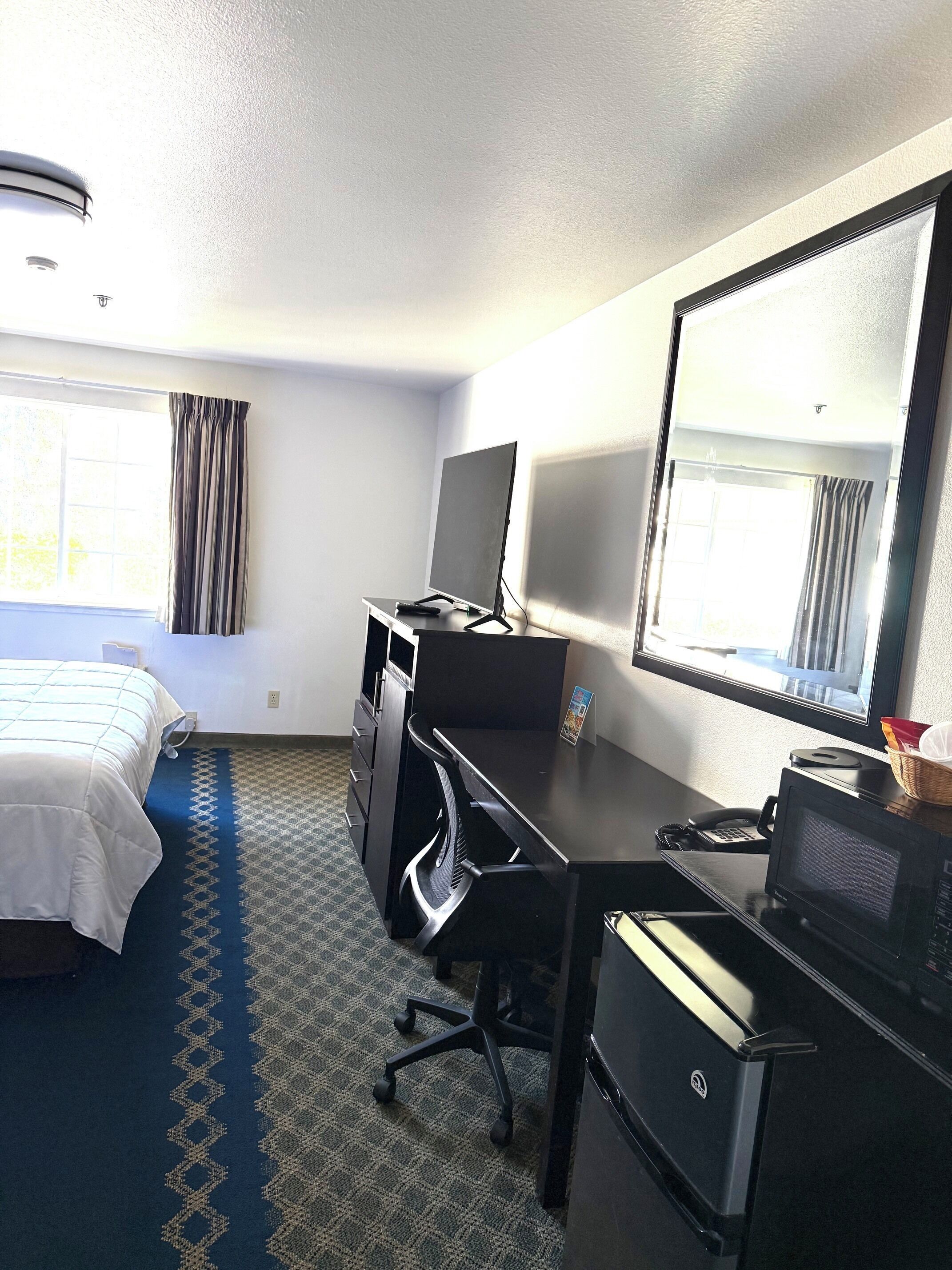 A hotel room with a bed, desk, computer, and microwave.
