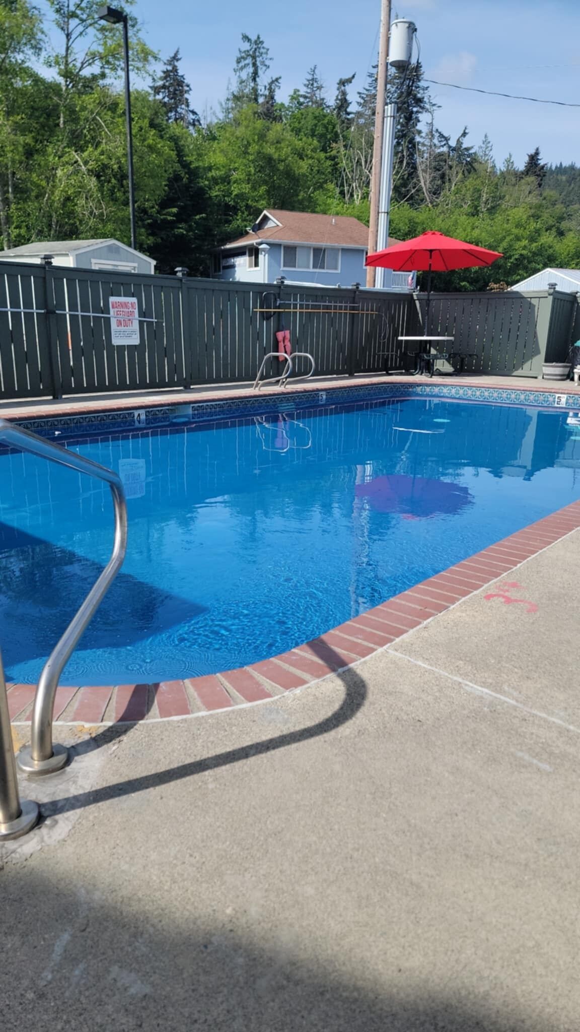 A swimming pool with a metal ladder, surrounded by a brick border and a wooden fence.