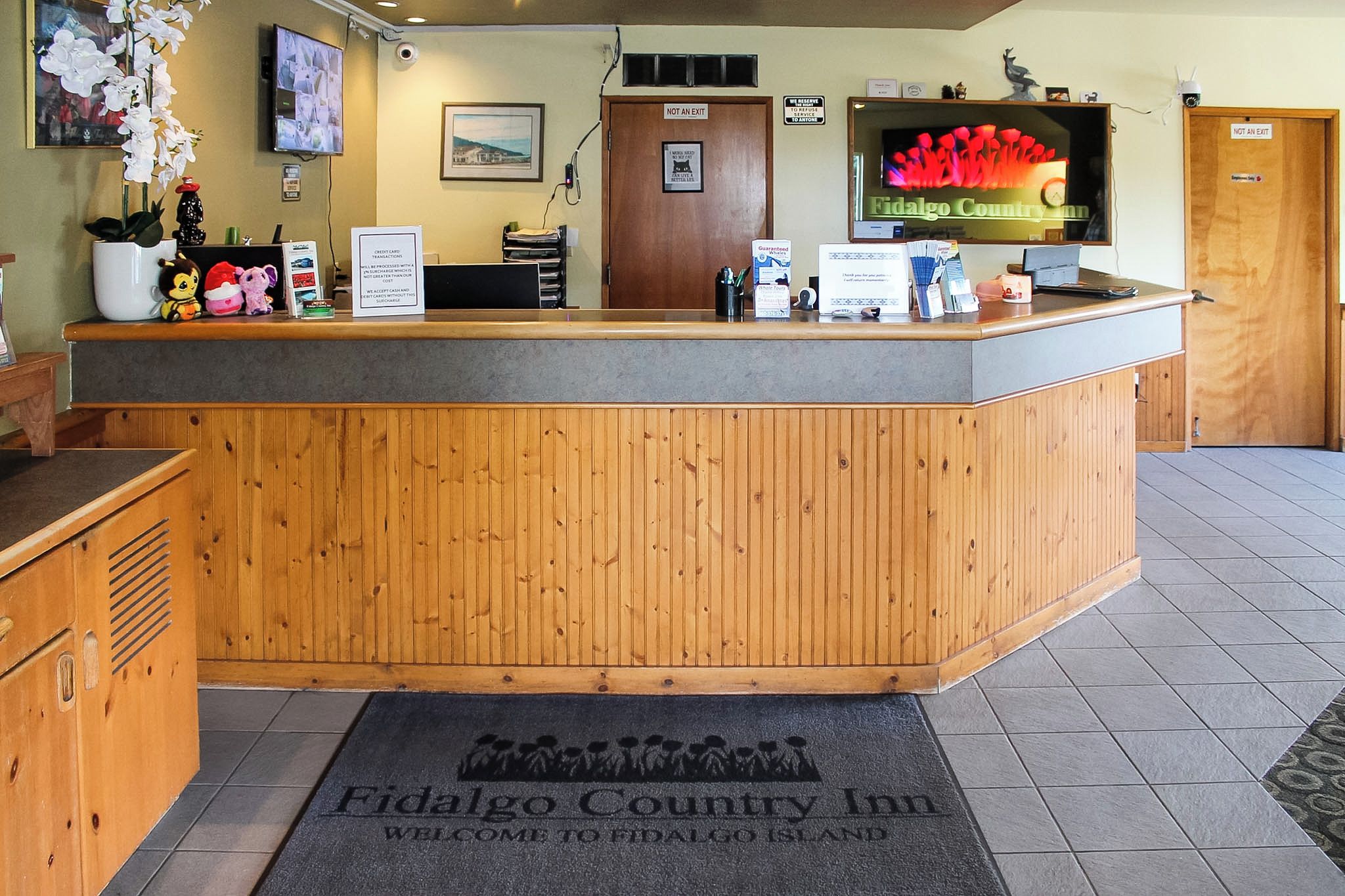 A reception desk with a wooden finish, a television mounted above it, and a welcome mat at the entrance.