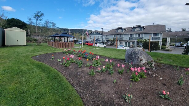 A residential area with a gazebo, a large rock, and a flower bed with pink flowers. - Fidalgo Country Inn (Anacortes)