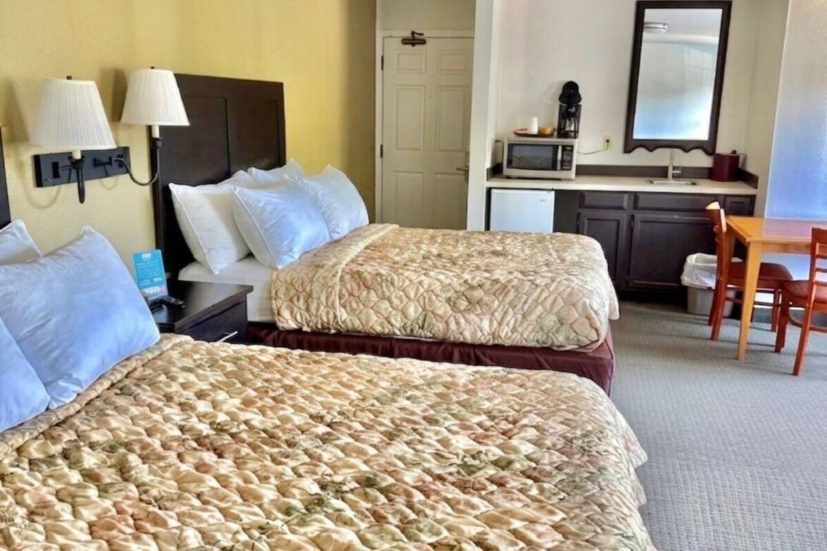 Quarto de hotel com duas camas, uma mesa, micro-ondas e uma pequena cozinha equipada.