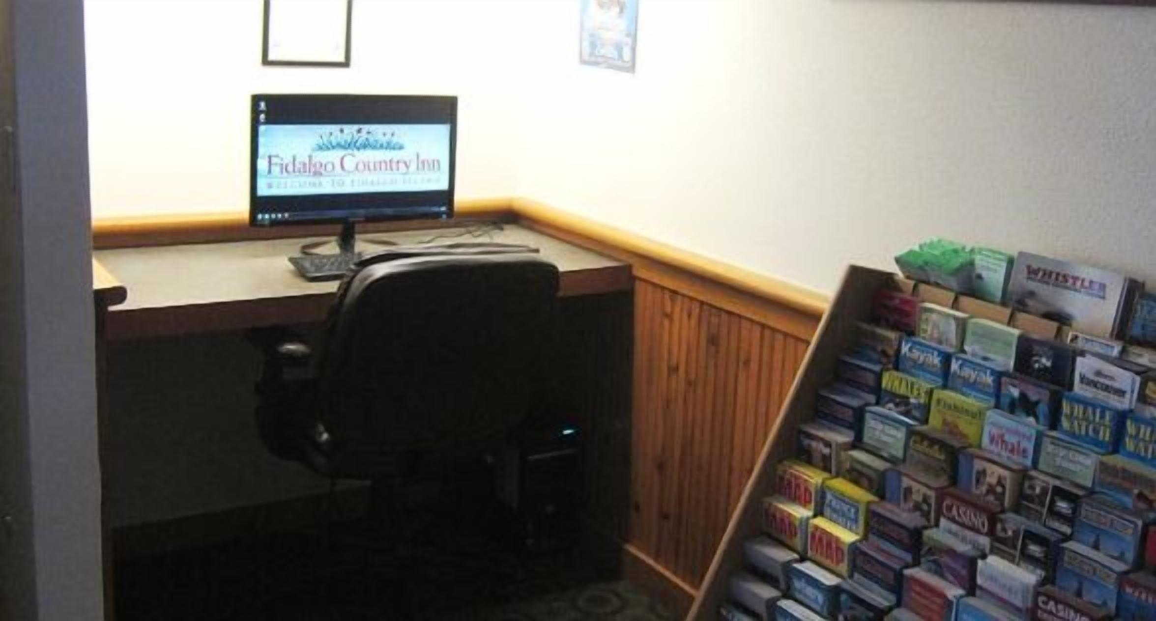 A desk with a computer, a chair, and a wall with a framed picture. There is a stack of books on the right side.