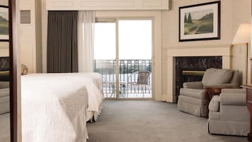 Habitación de hotel con cama, zona de estar con sillones, chimenea y balcón con vistas.
