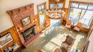 A spacious living room with a fireplace, comfortable seating, and large windows offering views of the outdoors. - Fairhaven Village Inn (Bellingham)