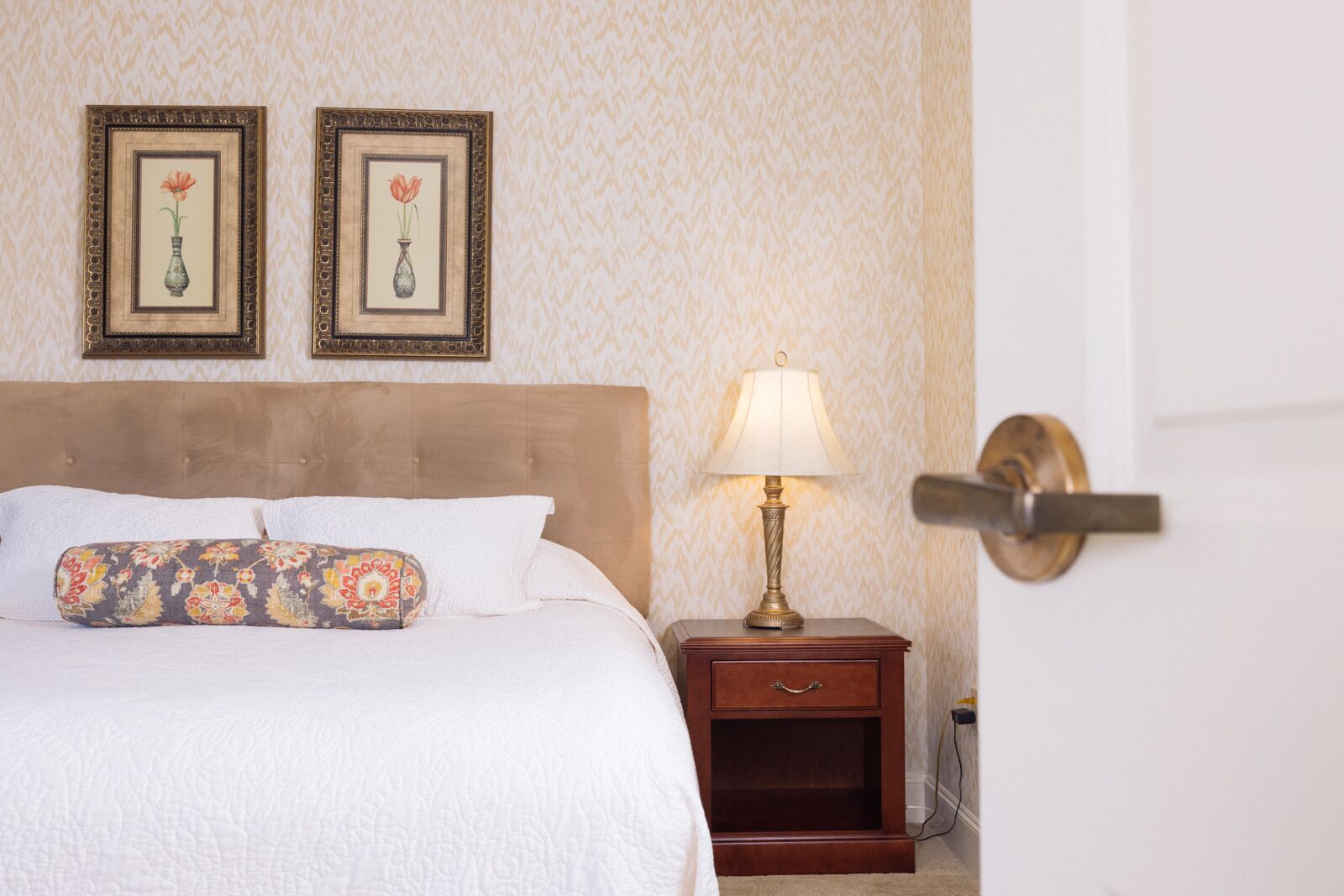 Une chambre d’hôtel avec un lit, une table de chevet avec une lampe et deux tableaux représentant des motifs floraux, accrochés au mur.