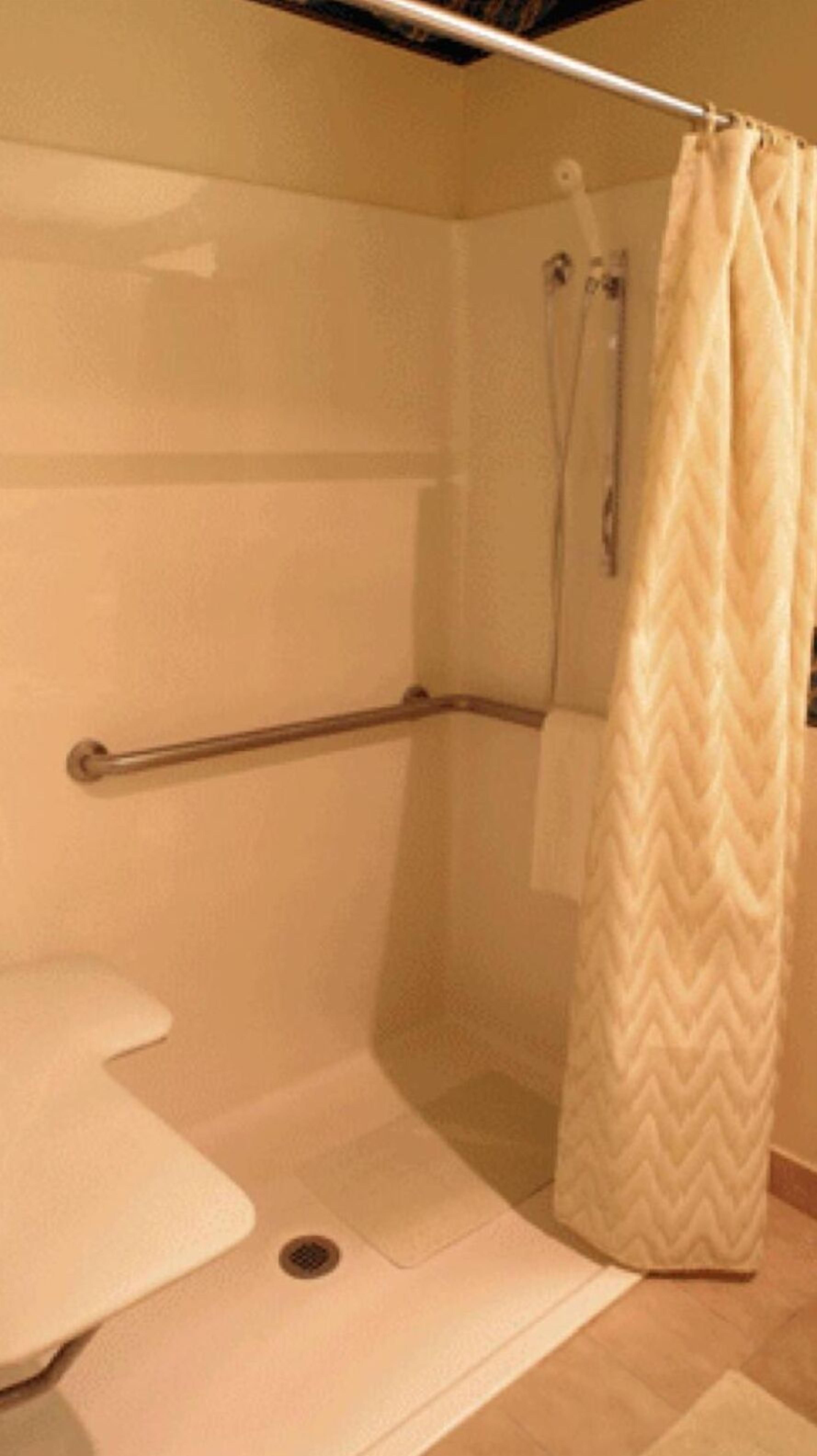 A small, enclosed shower area with a white shower curtain, a grab bar, and a white toilet.