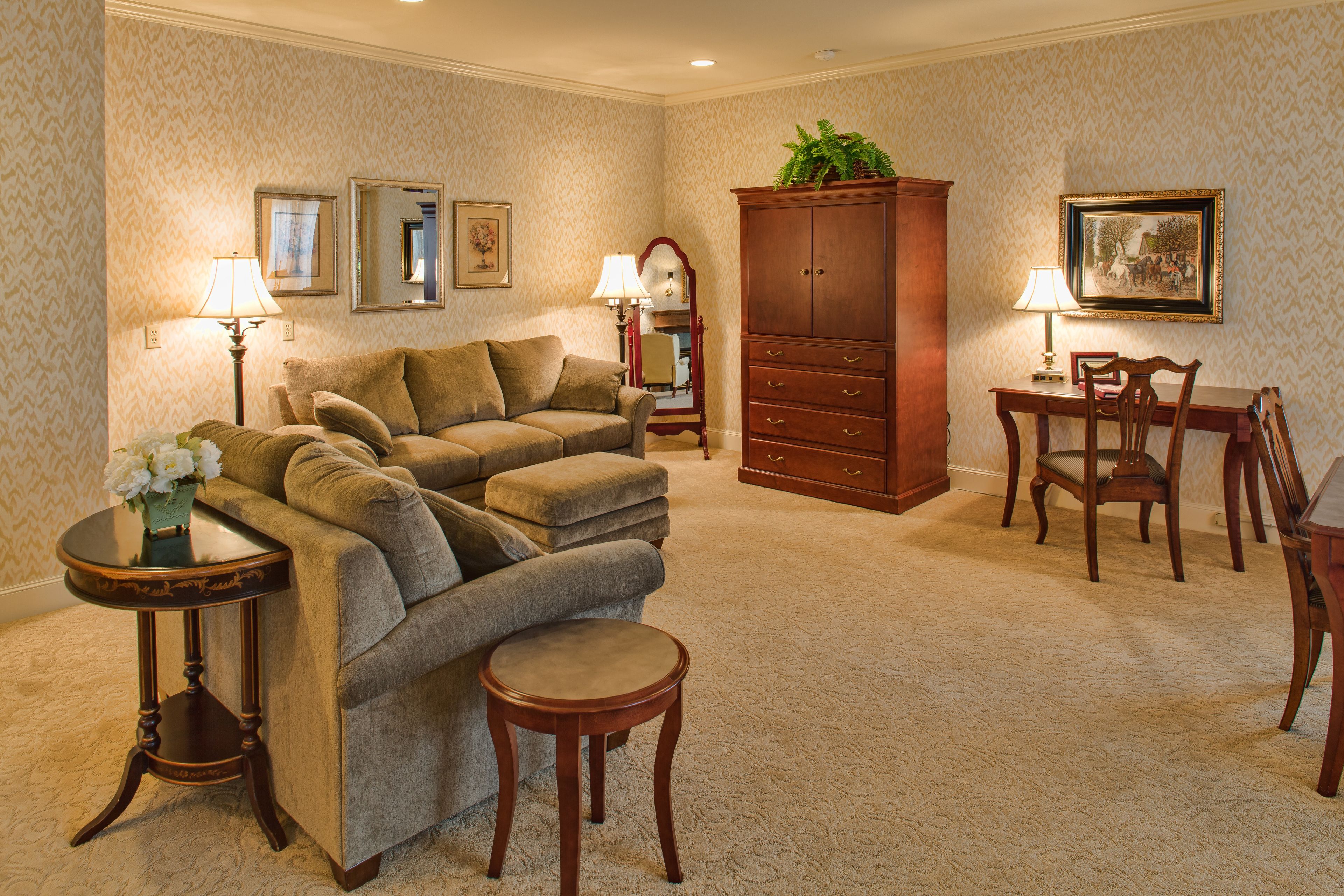 A living room with a sofa, a dining table with chairs, a cabinet, and a small table with a lamp and flowers.