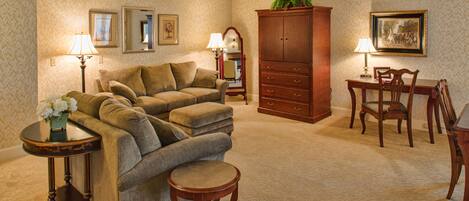 A living room with a sofa, a dining table with chairs, a cabinet, and a small table with a lamp and flowers.