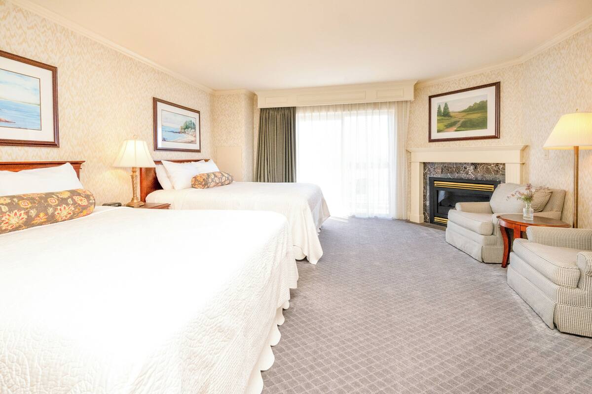 A hotel room with two beds, a sofa, a fireplace, and framed pictures on the walls.