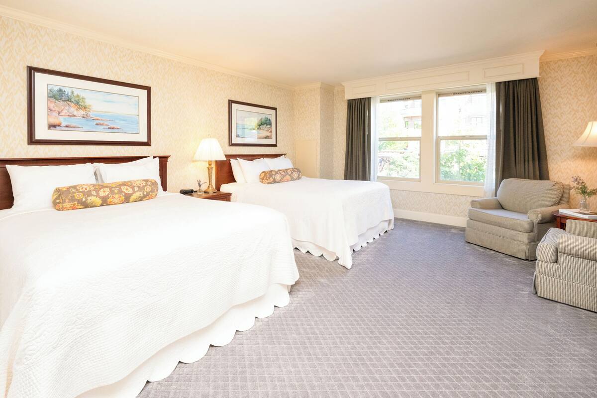 A hotel room with two beds, a sofa, a window with curtains, and framed artwork on the walls.