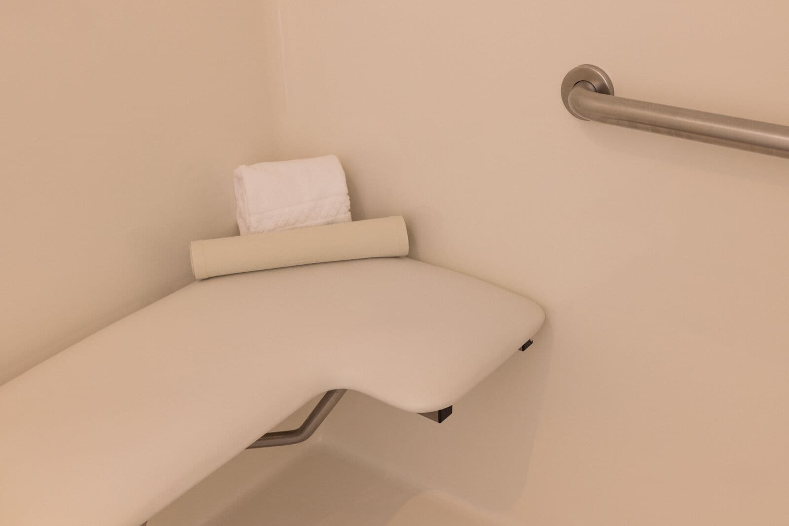 A corner of a room with a white towel on a shelf, a metal grab bar, and a white wall.
