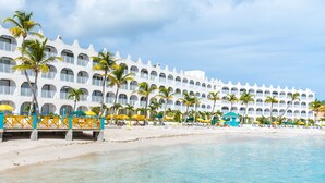 Un hotel frente al mar con varios balcones, palmeras y sombrillas de playa.