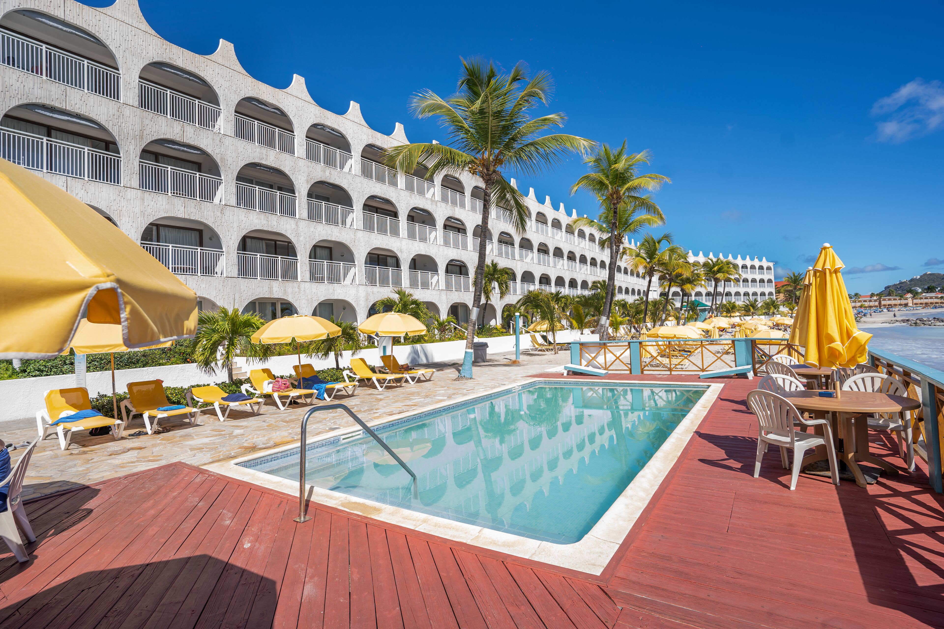 A pool area with lounge chairs and umbrellas, a pool, and a building with balconies.