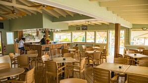 Un restaurante con mesas y sillas de madera, una zona de bar y amplios ventanales con vistas al exterior.