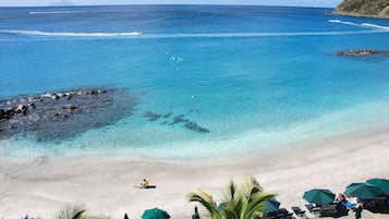 Na praia, areia branca, espreguiçadeiras, guarda-sóis