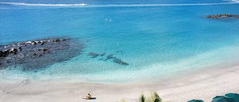A beach with clear blue water, a sandy shore, and several lounge chairs with umbrellas.