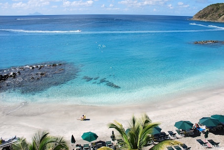 A beach with clear blue water, a sandy shore, and several lounge chairs with umbrellas.