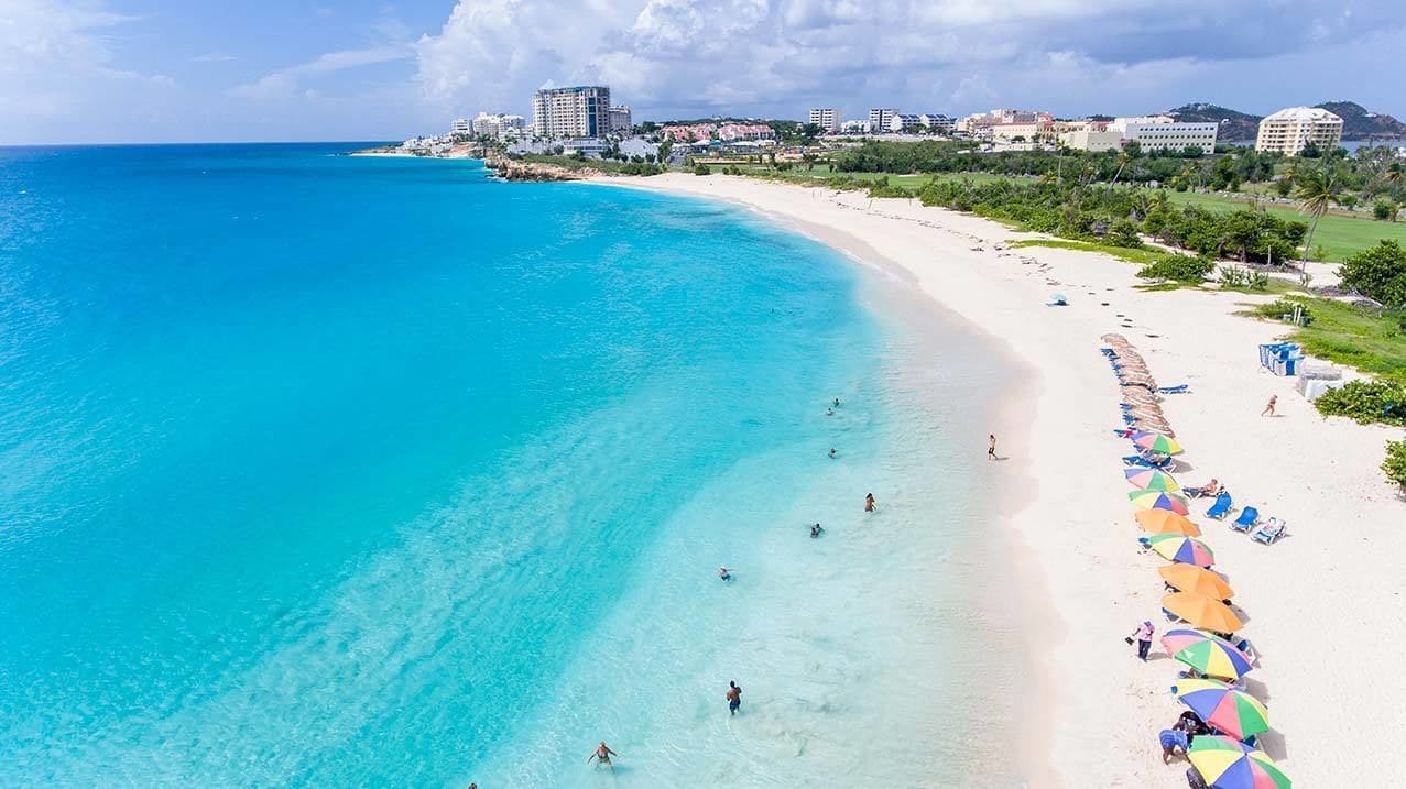 A beach with clear turquoise waters, a sandy shore, and a row of colorful umbrellas.