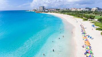 A beach with clear turquoise waters, a sandy shore, and a row of colorful umbrellas.