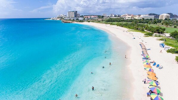 A beach with clear turquoise waters, a sandy shore, and a row of colorful umbrellas.