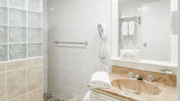 A bathroom with a glass shower enclosure, a white toilet, a sink with a mirror, and a towel rack.
