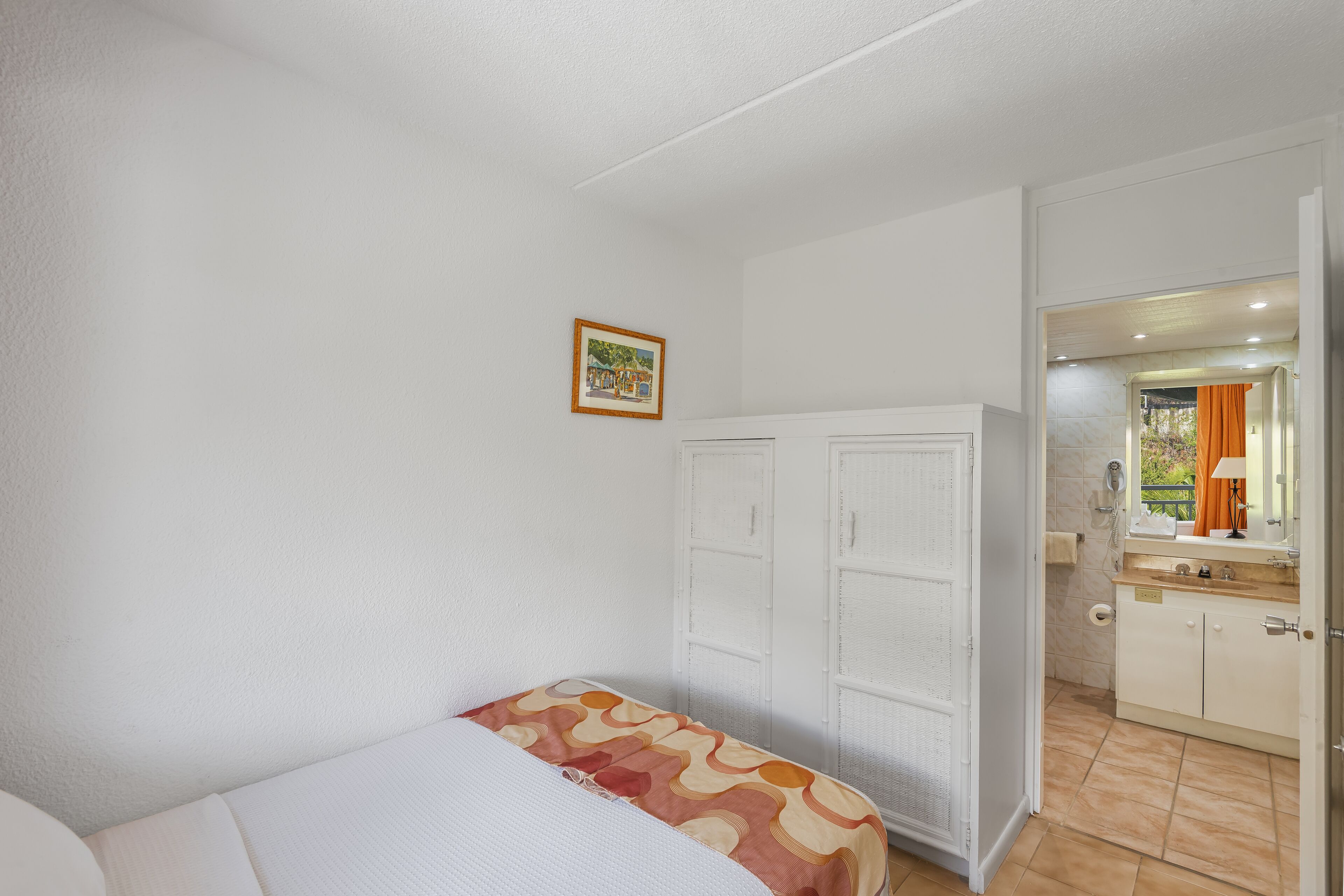 A bedroom with a bed, a wardrobe, a bathroom with a mirror, and a small picture on the wall.