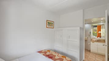 A bedroom with a bed, a wardrobe, a bathroom with a mirror, and a small picture on the wall.