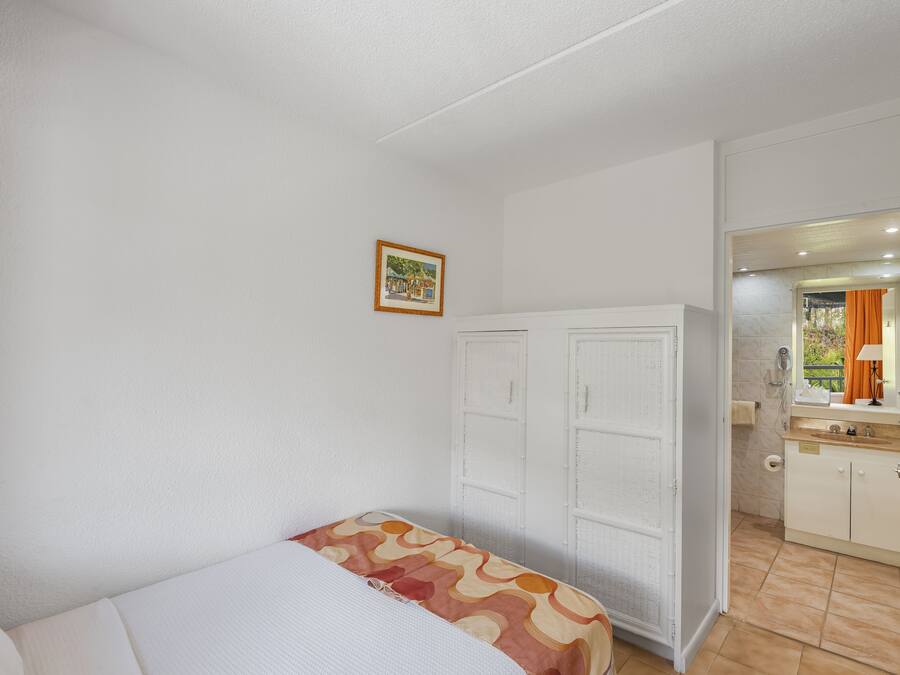 A bedroom with a bed, a wardrobe, a bathroom with a mirror, and a small picture on the wall.