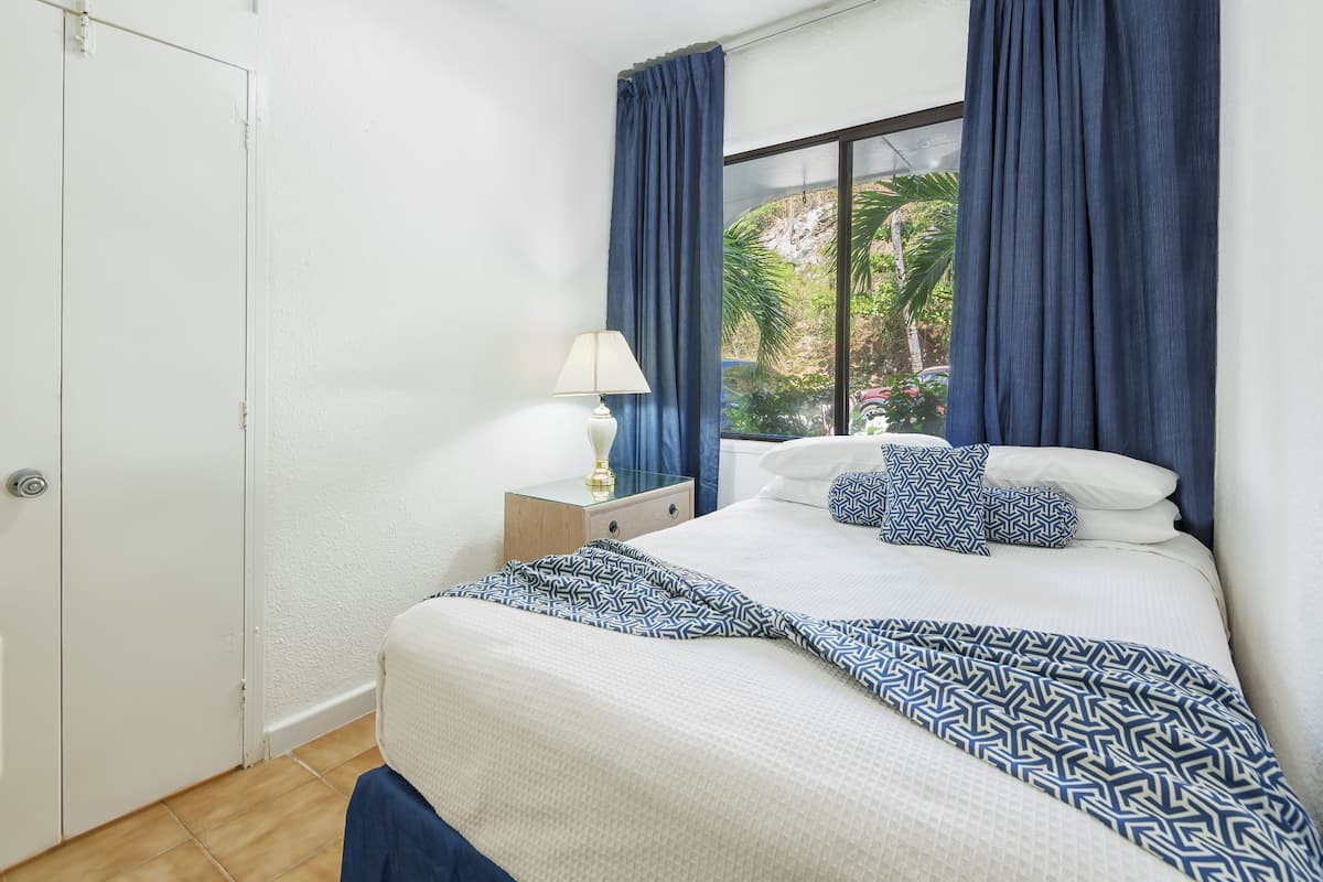 Une chambre à coucher avec un lit, une table de chevet, une lampe et une fenêtre avec des rideaux.
