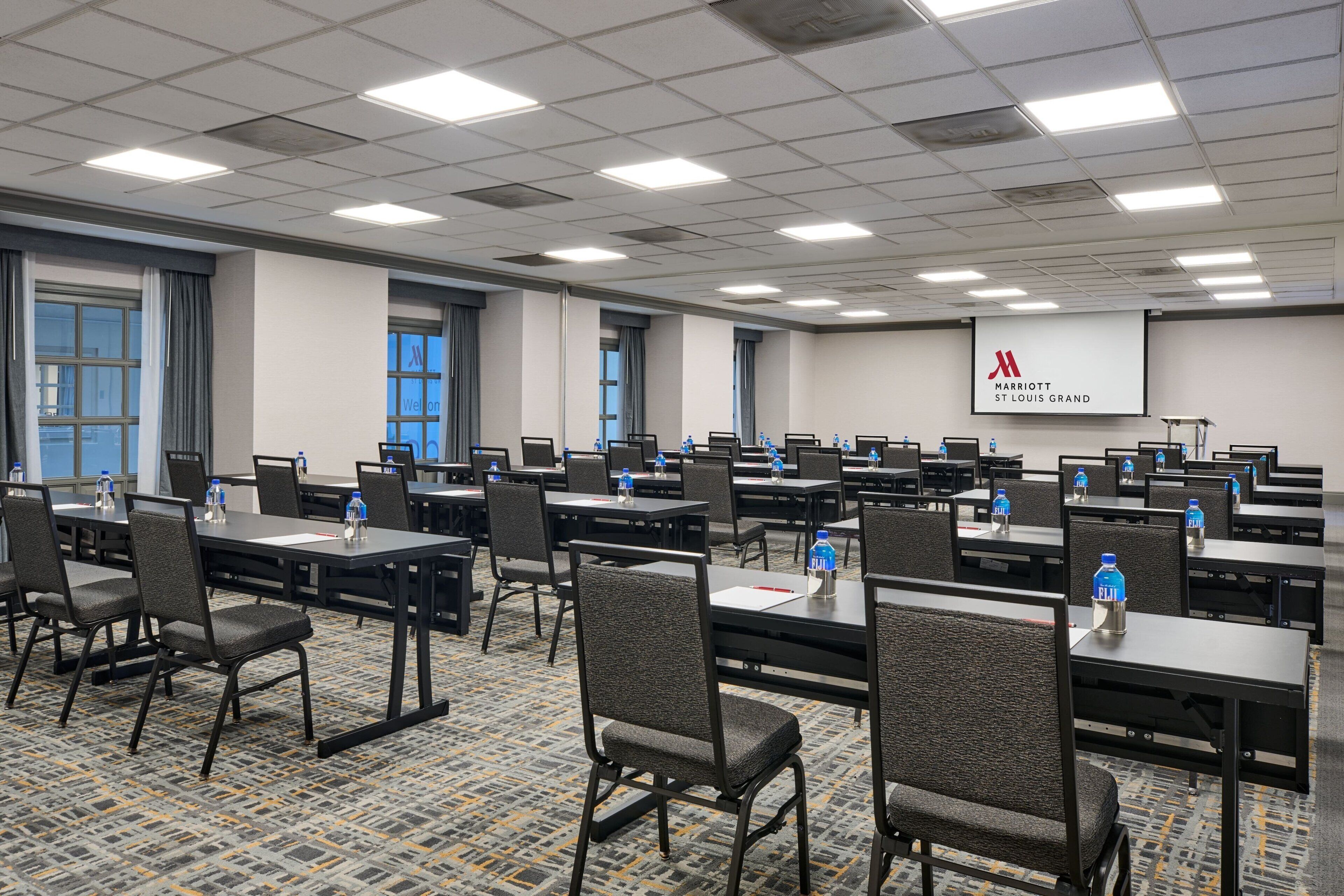 A conference room with multiple tables and chairs, water bottles on each table, and a Marriott logo on the wall.