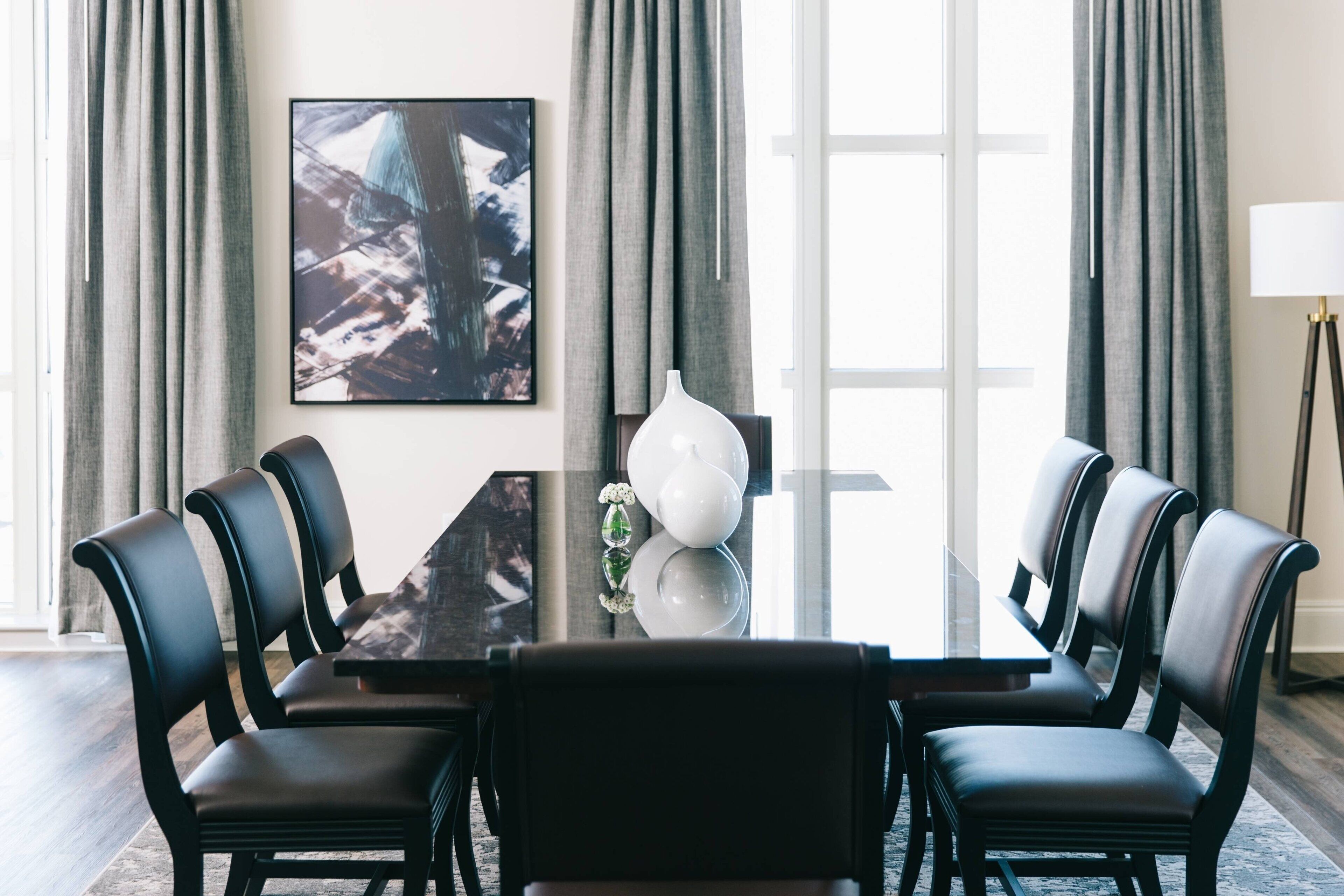 A conference room with a glass table, black chairs, a white vase, and a painting on the wall.