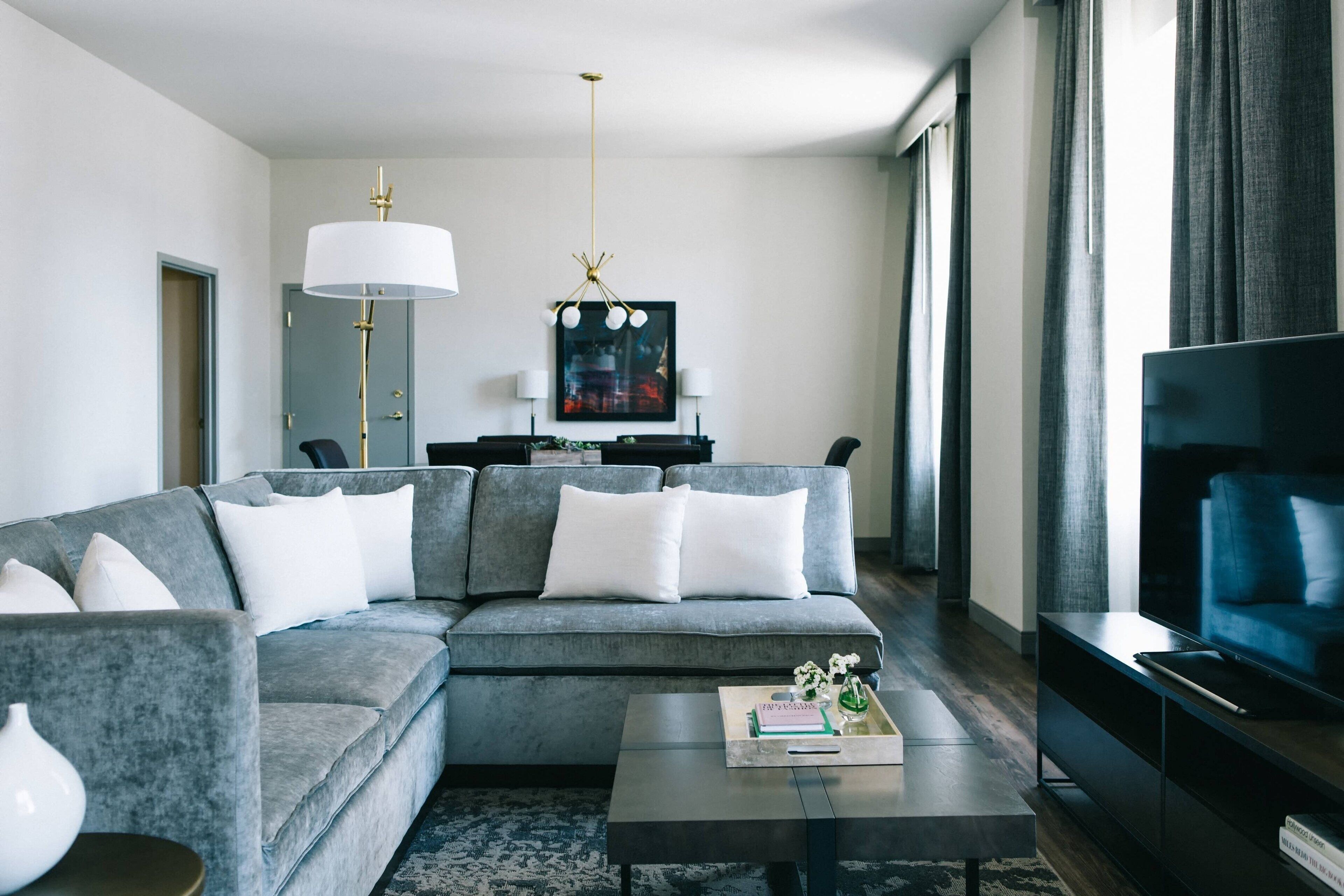 Ein modernes Wohnzimmer mit einem grauen Ecksofa, einem Couchtisch, einem Flachbildfernseher und einer Chandelüster.