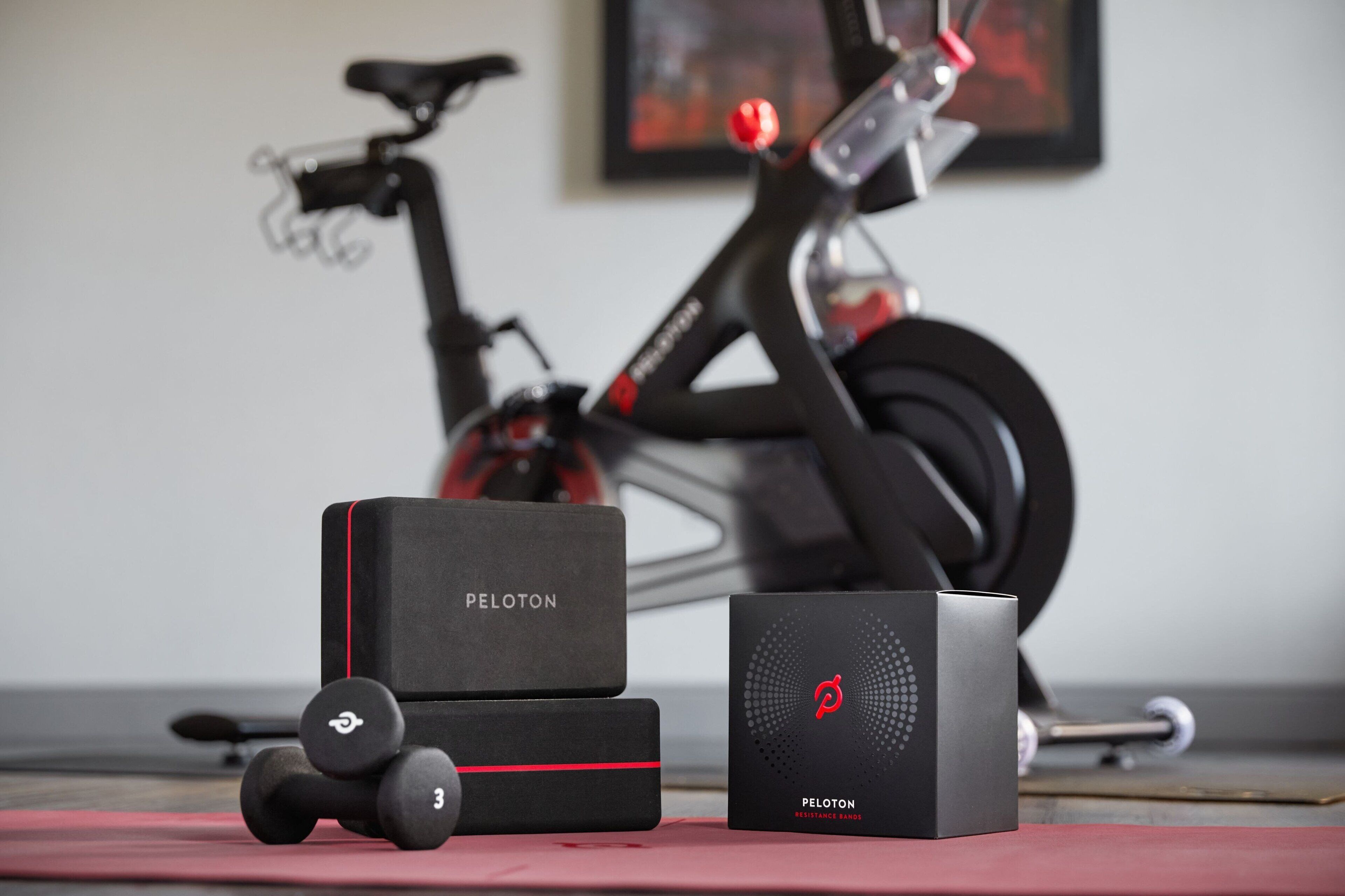 A Peloton exercise bike, two Peloton resistance bands, and a Peloton resistance trainer on a red mat.
