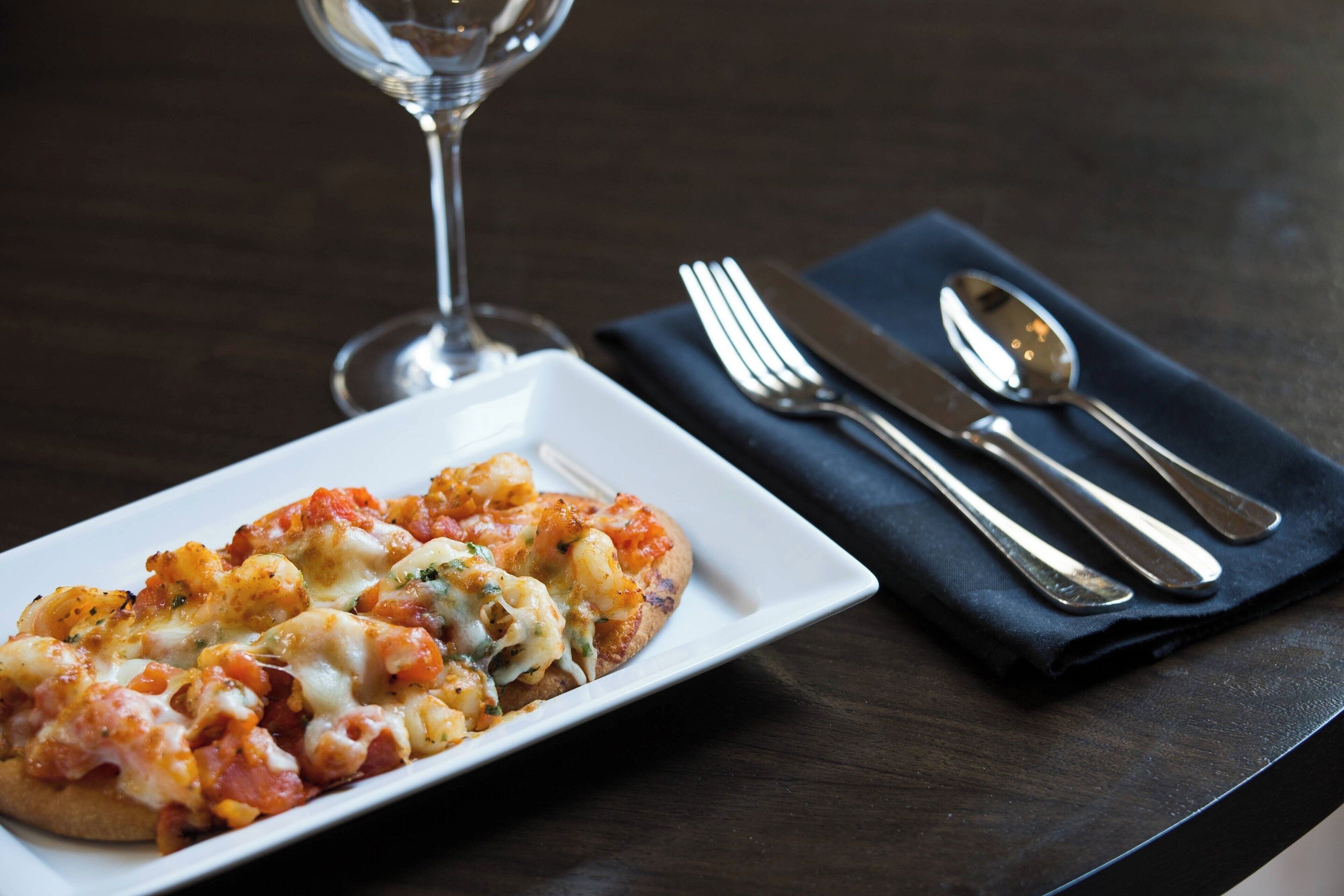 A plate of food on a table with a wine glass and cutlery.