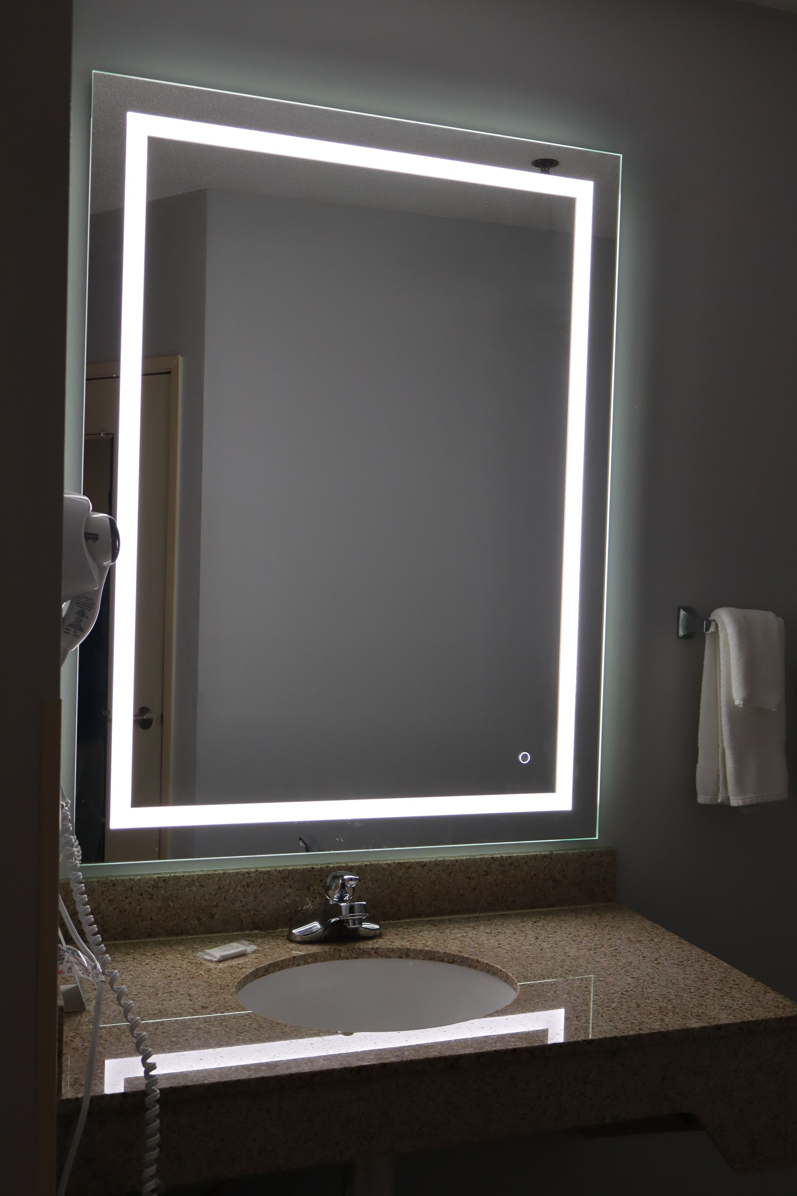 A bathroom with a large mirror, a sink, and a towel rack.