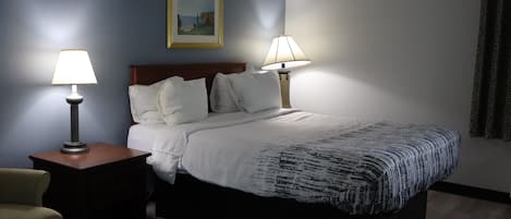 A hotel room with a bed, two bedside lamps, a chair, a framed picture on the wall, and a window with curtains.