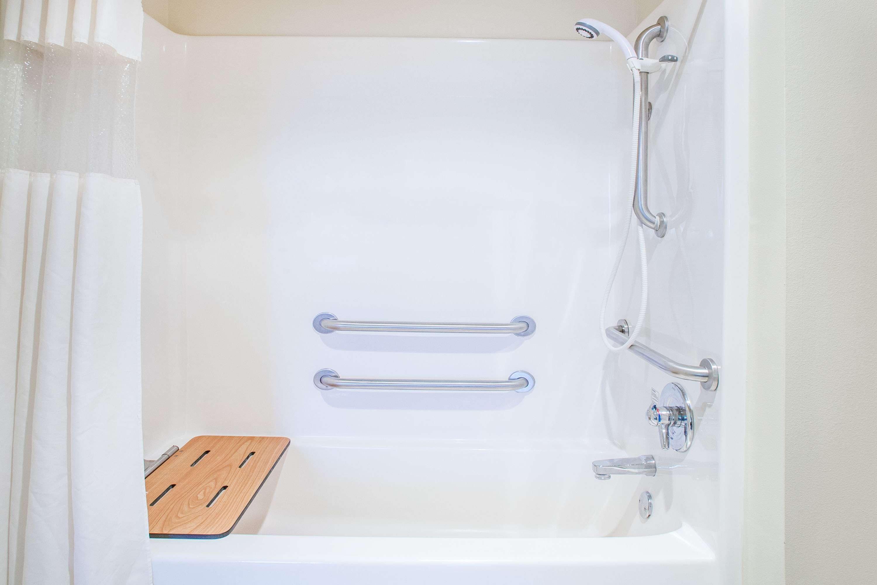 Una vasca da bagno bianca con due maniglie di sostegno, uno scalino in legno e un soffione.