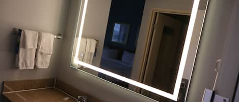 A bathroom with a large mirror, a sink, and towels on a rack.