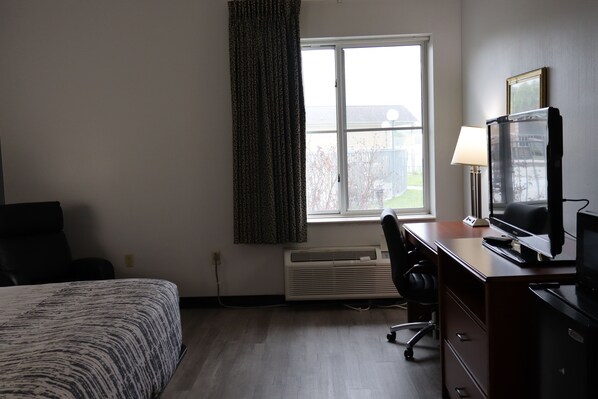 A hotel room with a bed, desk, chair, and window.
