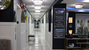 Un pasillo de hotel con un cartel, una recepción y una banca.