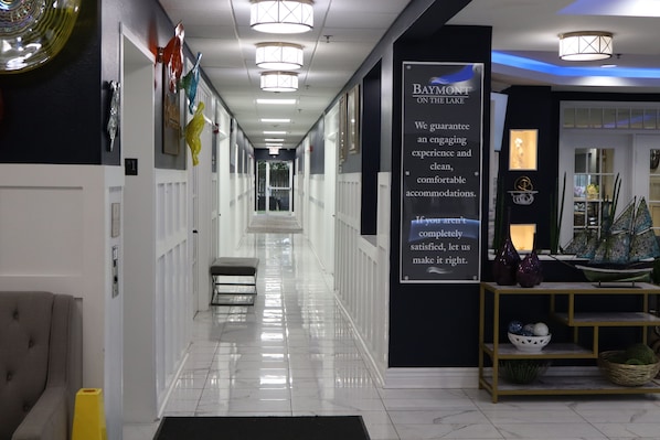 Un couloir d’hôtel avec un panneau indicateur, un comptoir de réception et un banc.