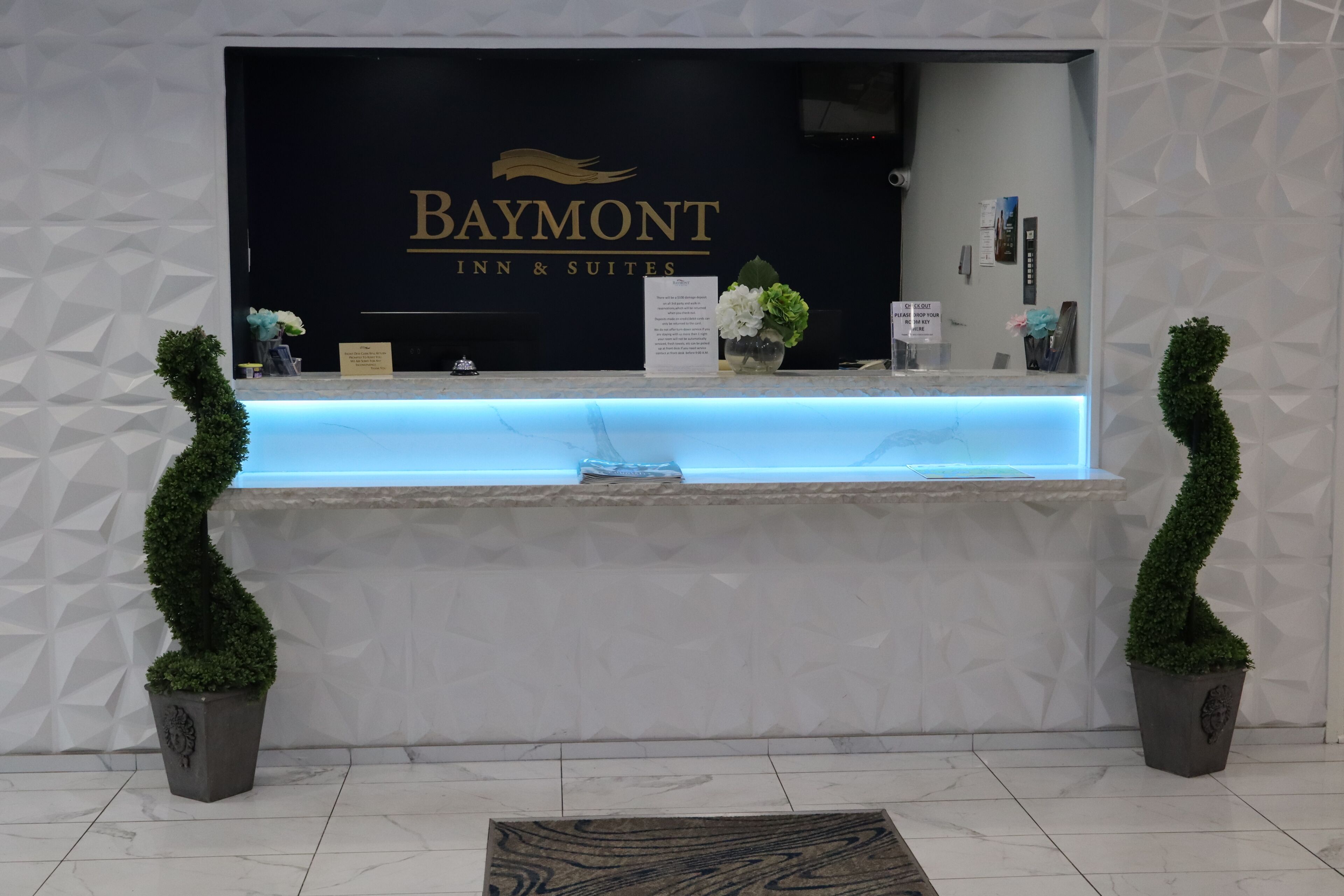 Un comptoir d’accueil avec une enseigne Baymont Inn & Suites, un comptoir bleu éclairé et deux plantes en pot.