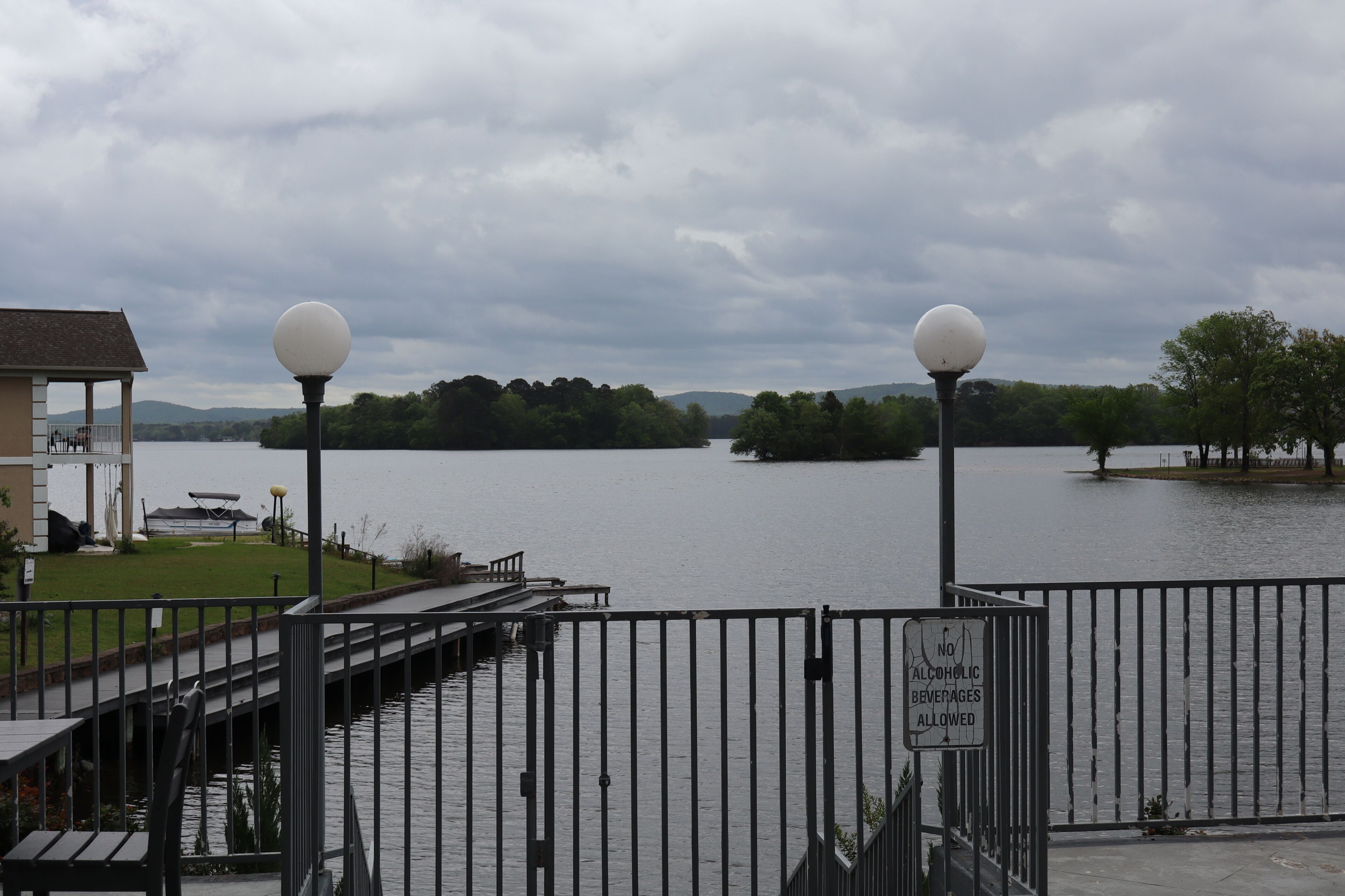 A waterfront view with a no alcohol beverages allowed sign, a dock, and a building with a covered area.