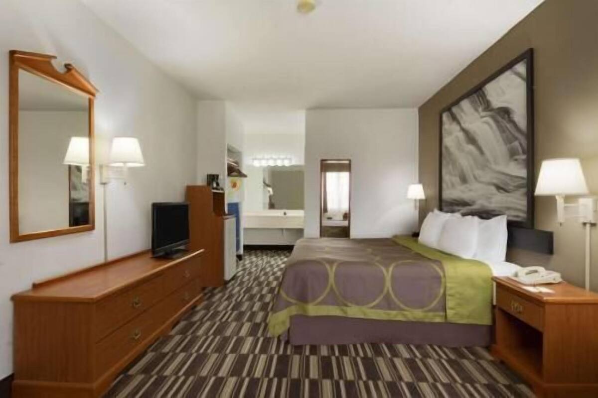 Una habitación de hotel con una cama, un escritorio, un televisor, un espejo y un cuadro en la pared.
